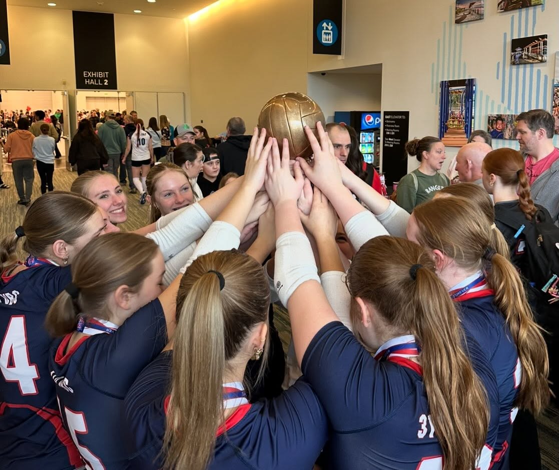 A 314 VBC team in navy jerseys huddled in a convention centre lobby with every hand raised to hold a gold volleyball trophy aloft.