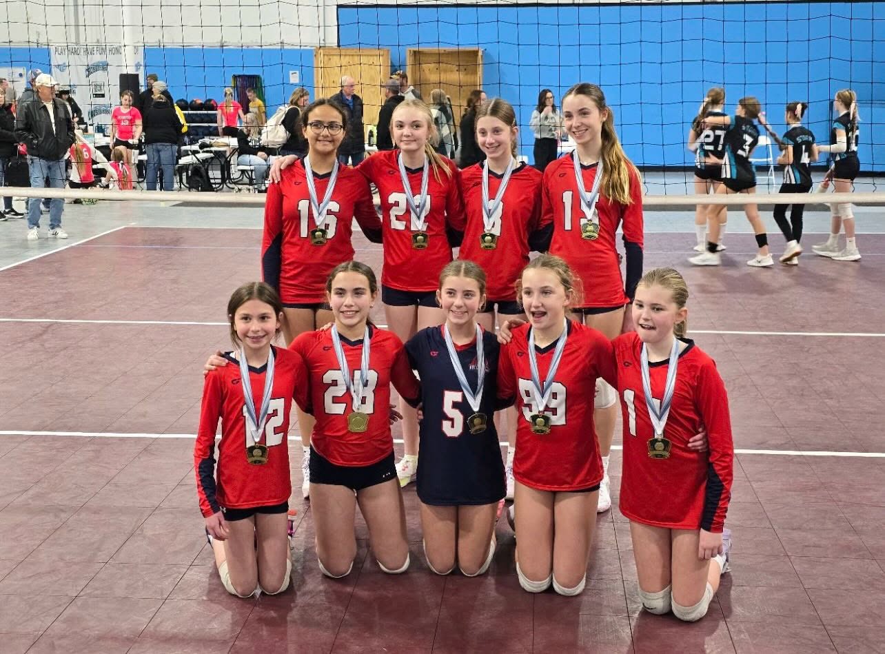 Nine young 314 VBC players in red jerseys, four standing and five kneeling, all wearing gold medals beside a tournament court.